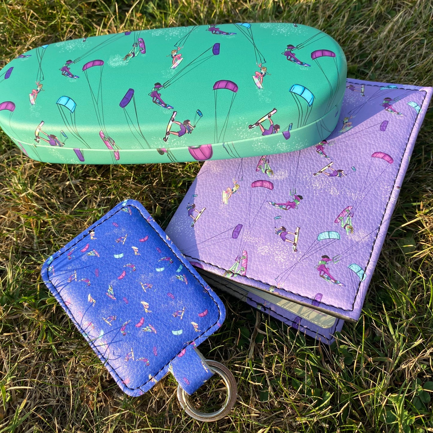 Image includes a green glasses case, purple leather passport cover, and blue leather keyring.