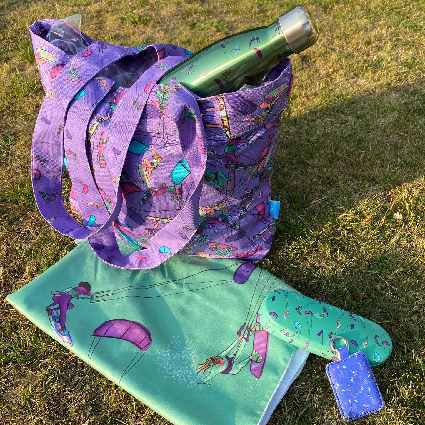 Purple tote bag with other Bellis Kitesurfing accessories: green water bottle, green microfibre towel, green glasses case, blue/ green leather keyring