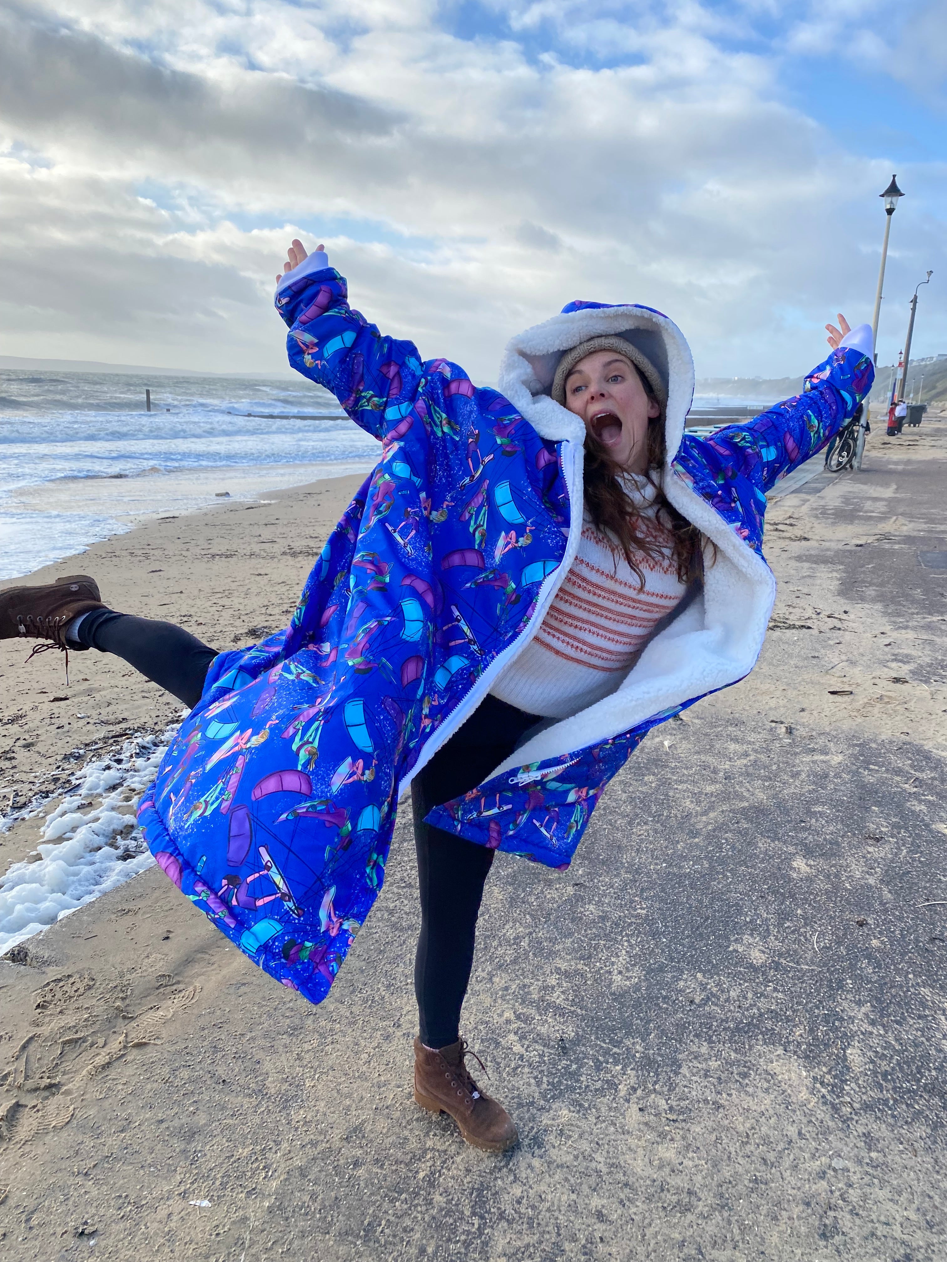 Women wearing a colorful kitesurfing print waterproof changing dry robe coat on a beach with a blue sky.
